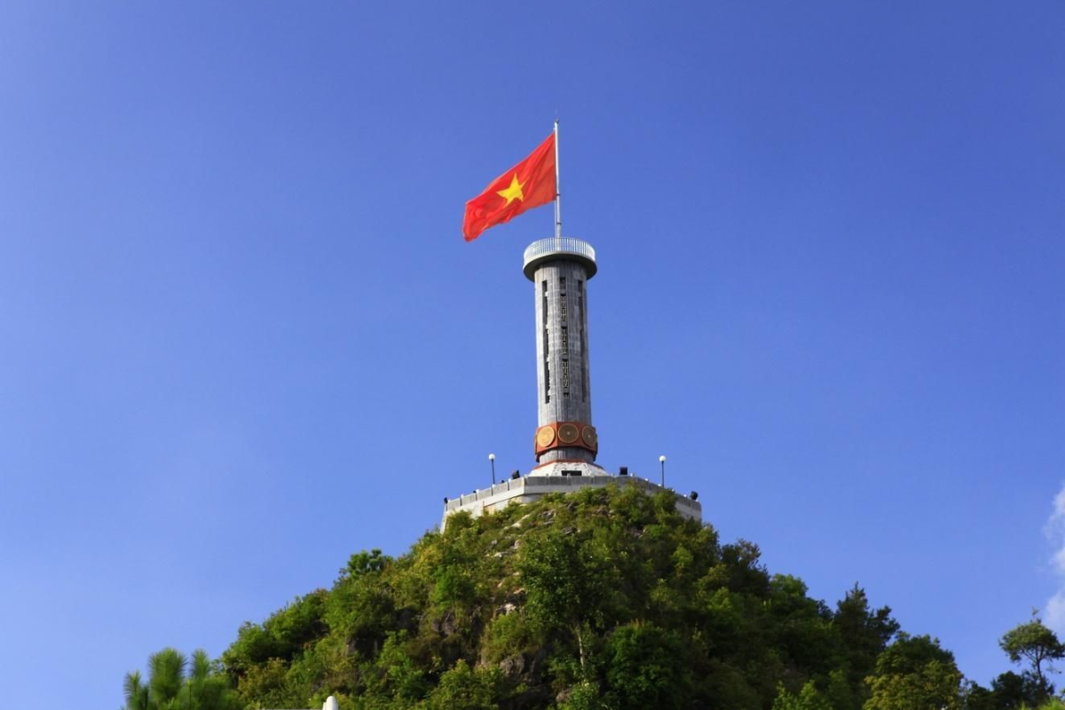 Vietnam’s national flag flying atop Lung Cu Flag Tower, marking the northernmost point of the country, surrounded by scenic mountains.